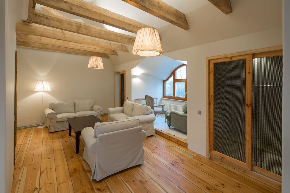 A cozy living room in Surrey, UK, featuring newly sanded and refinished pine plank floors. The room includes white sofas, a wooden coffee table, exposed wooden beams, and soft lighting. The floor sanding and refinishing were done by Mr Sander®.