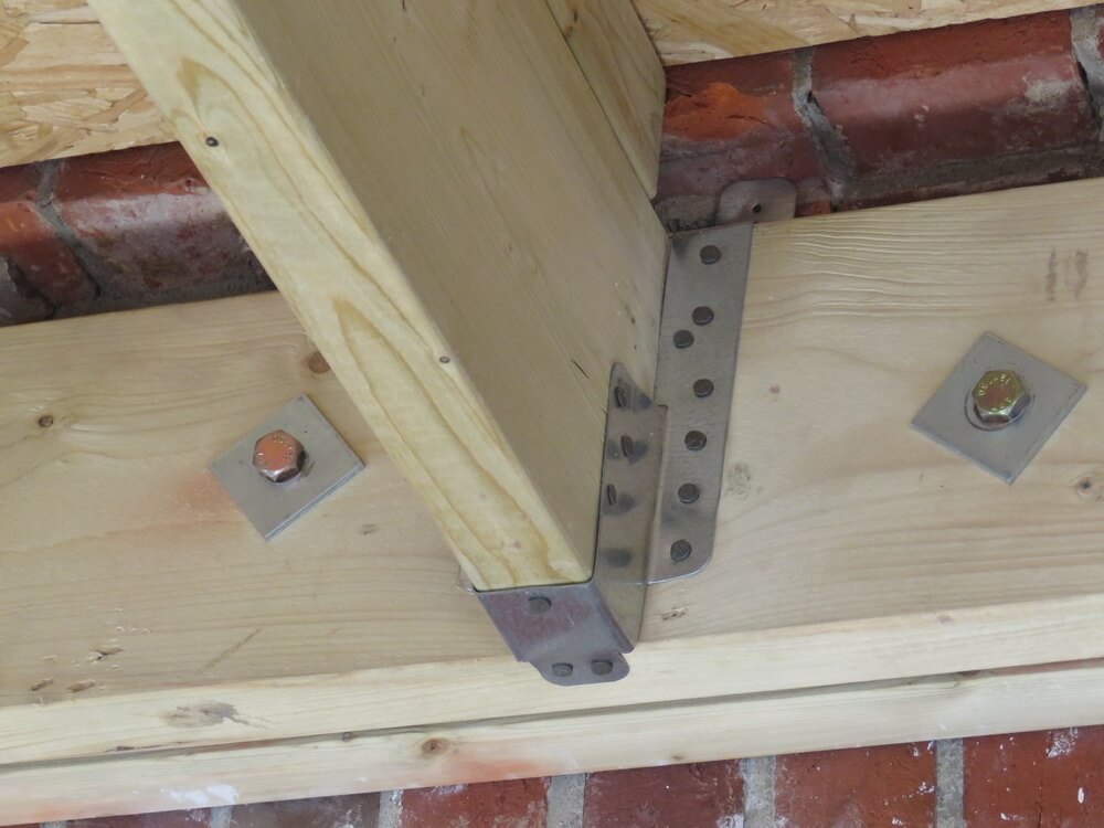 A close-up of wooden beams securely fastened with metal brackets and bolts, showcasing structural support in a flooring project.