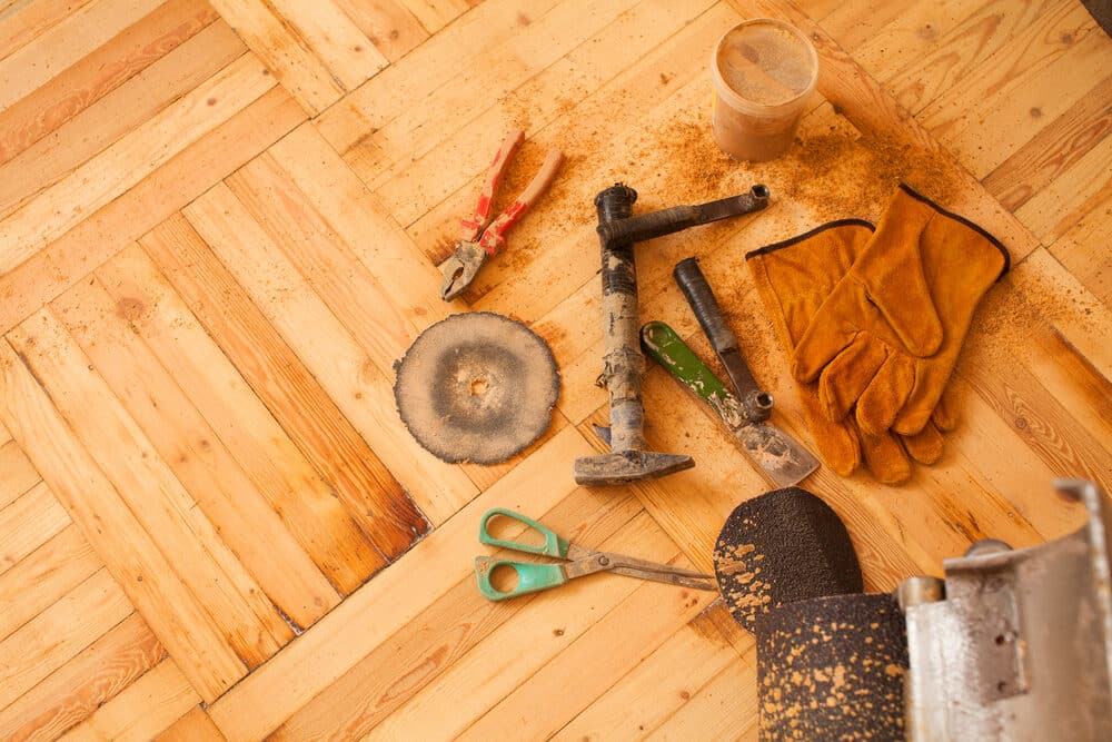 A collection of woodworking tools and a pair of gloves scattered on a wooden floor, with sawdust around