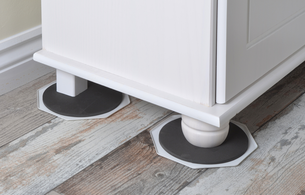 Two furniture sliders under the legs of a white cabinet on a wooden floor