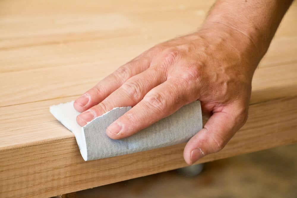 Hand sanding the edge of a wooden board with sandpaper.