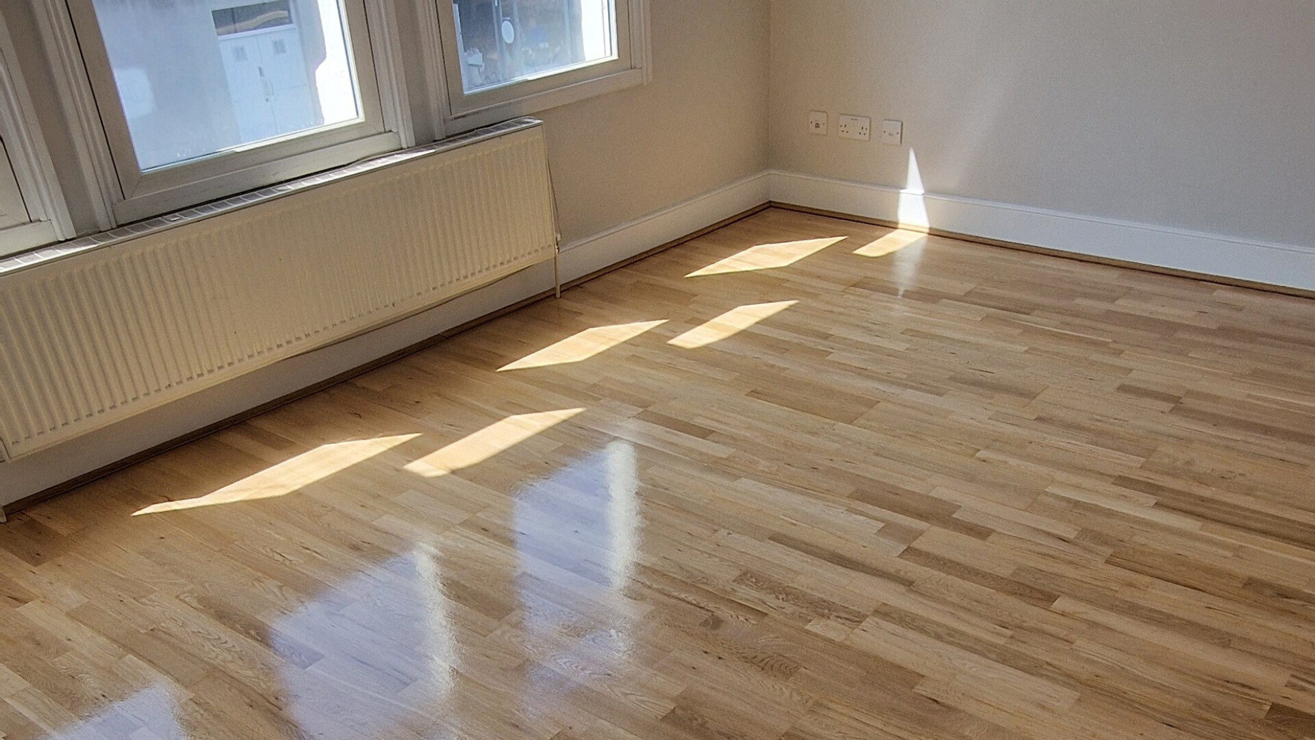 Bright room with engineered oak 3-strip hardwood floor in a low-sheen finish, illustrating a smooth, UFH-friendly surface within a guide on Solid Boards Over UFH.