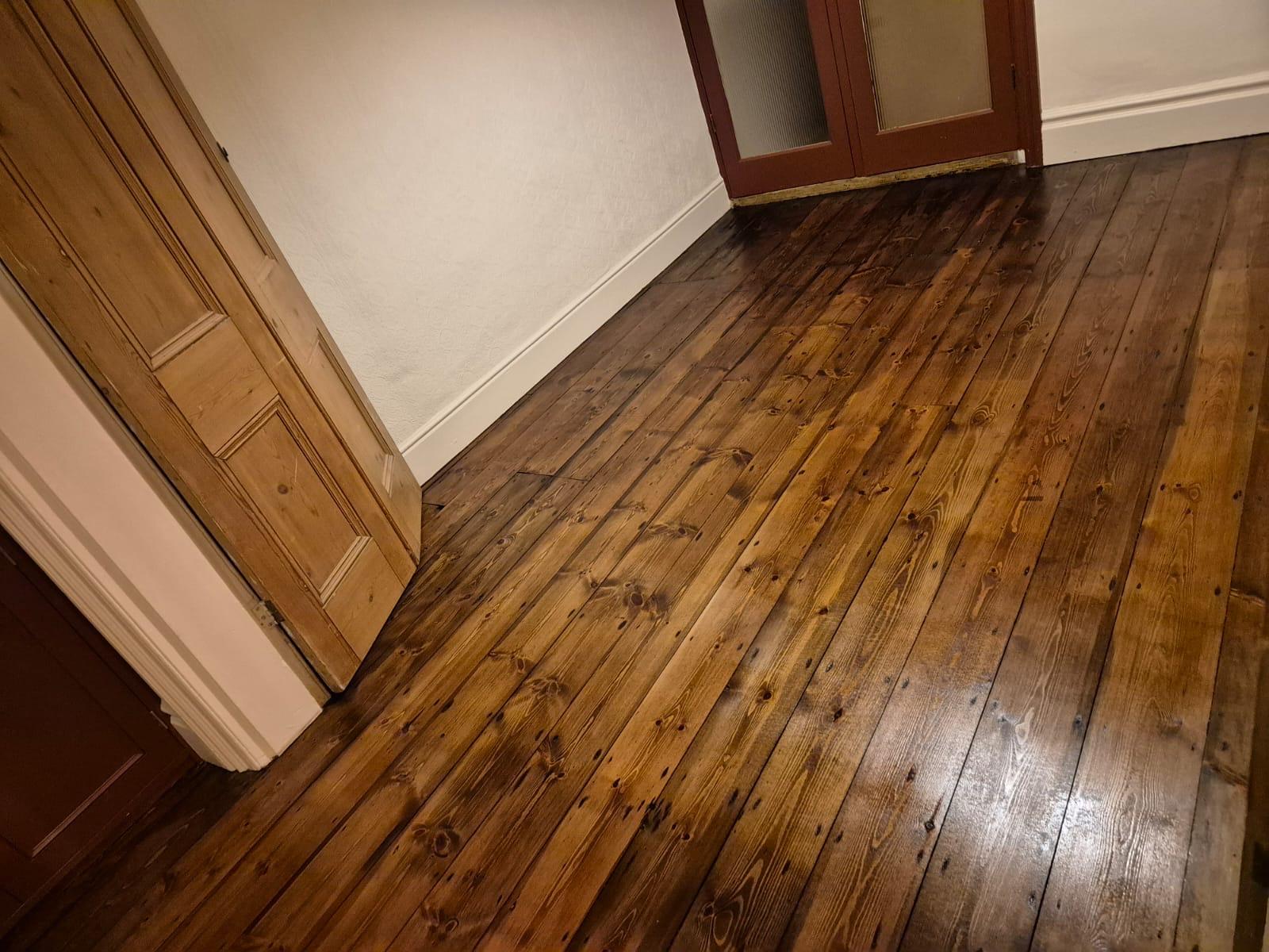 Solid Wood Floor Restoration showcasing rich, dark-stained solid pine floorboards in a hallway, with restored plank flooring running between wooden doors and white skirting.