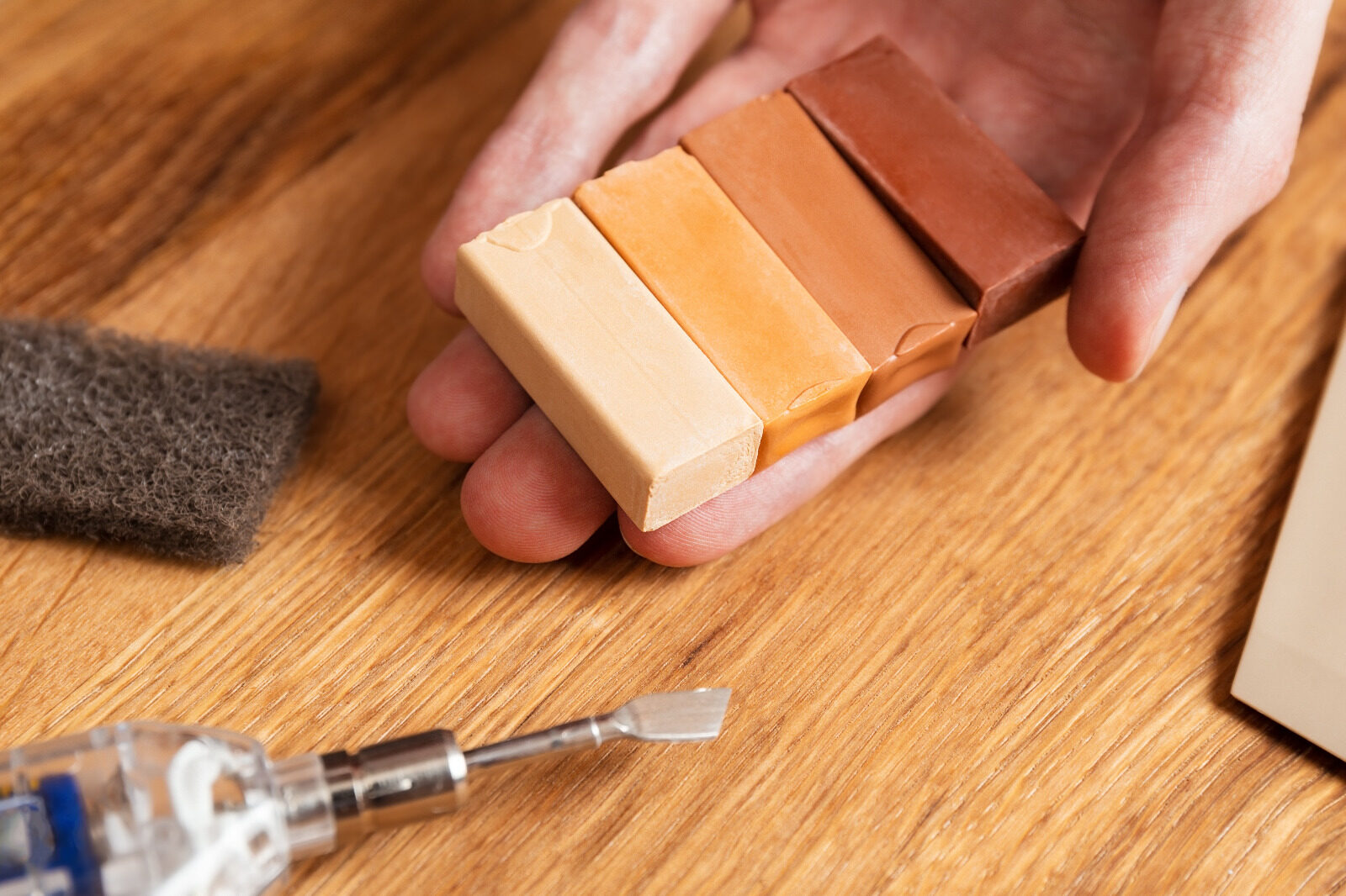 Spot Repair on oak hardwood plank floor with technician selecting colour-matched hard-wax filler sticks and hot knife for fine scratch and chip repair