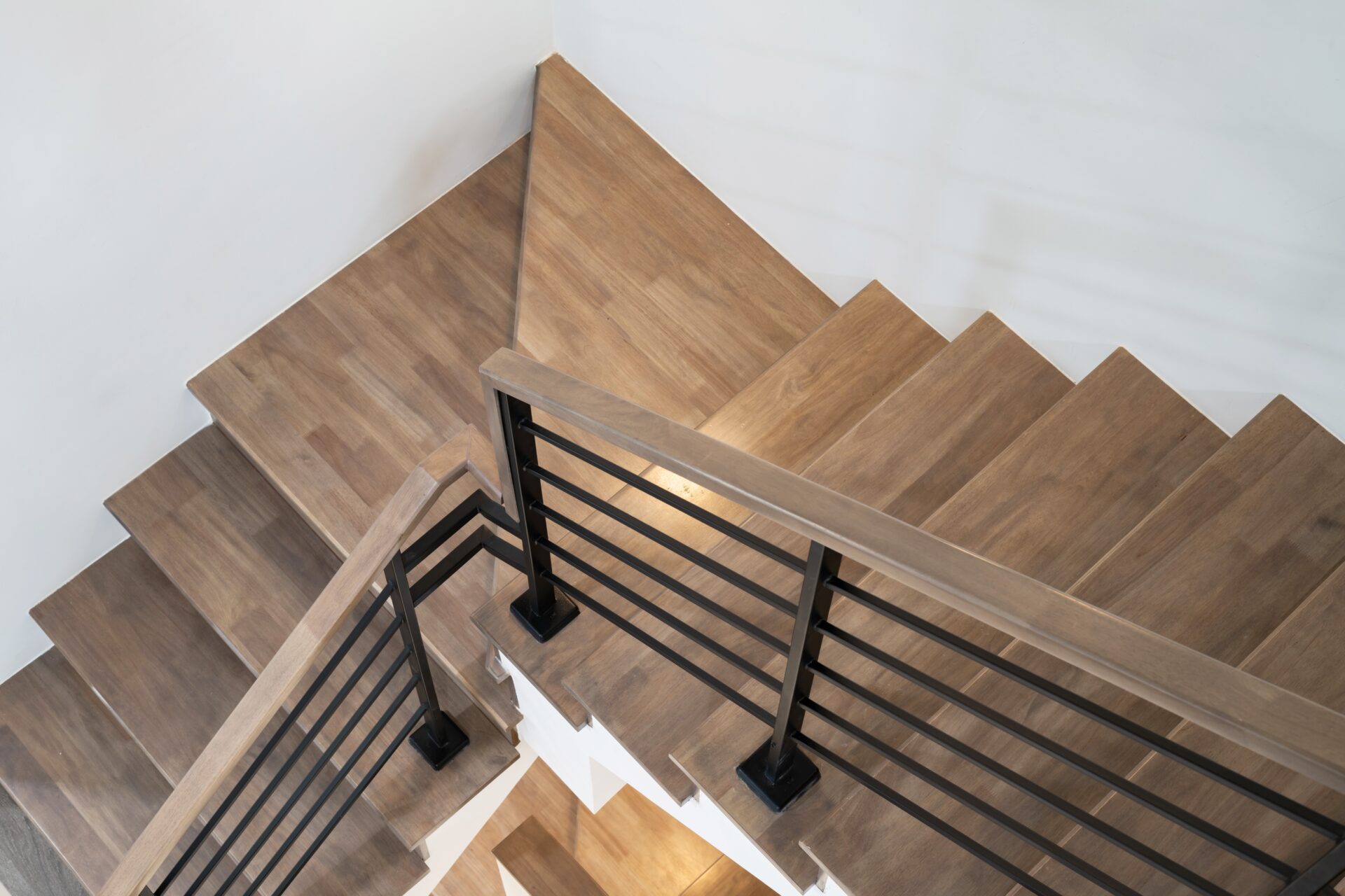A high-angle view of a Staircase Revival featuring light brown white oak hardwood treads and a sleek black metal horizontal railing.
