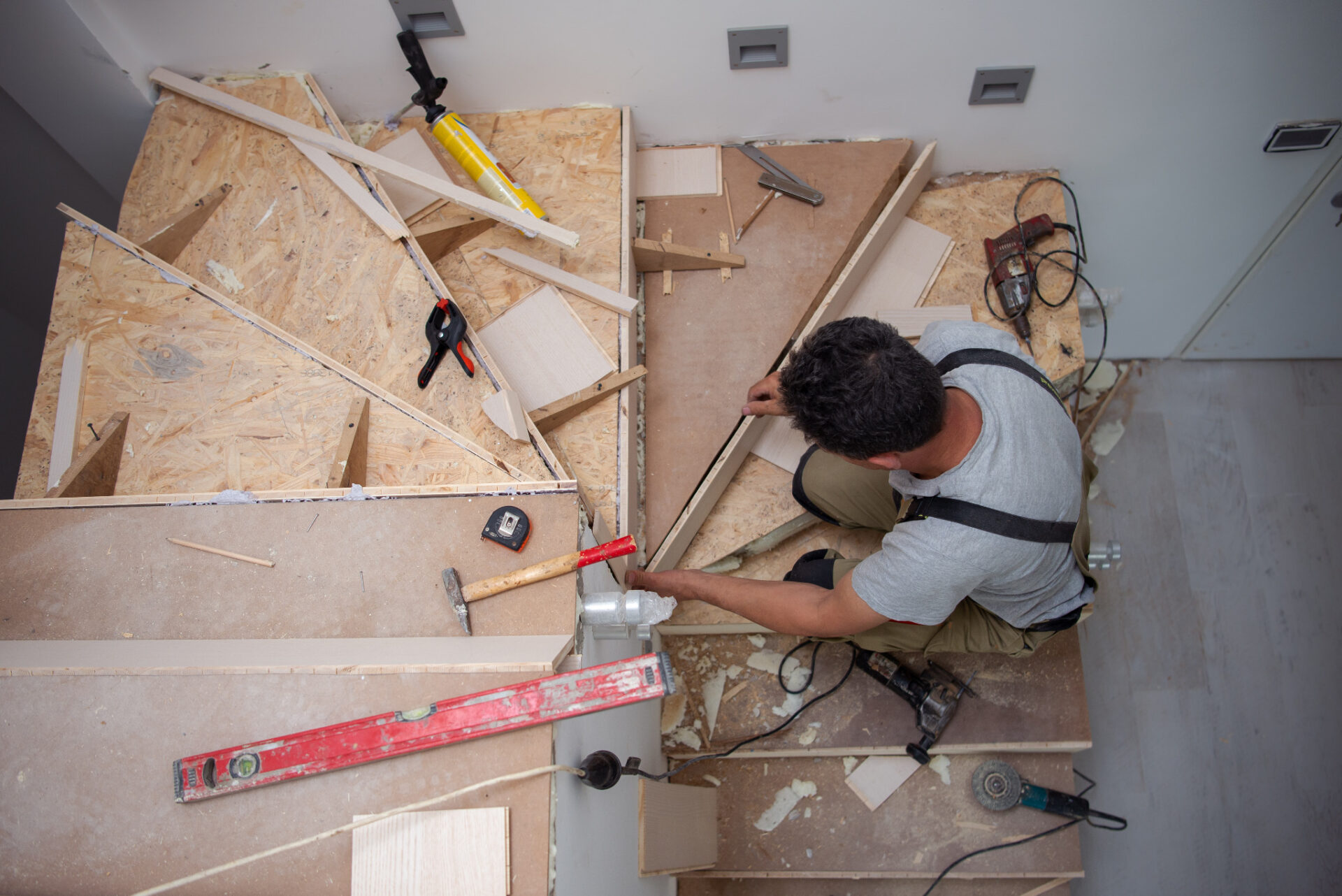 A carpenter performing a Staircase Revival by installing new oak wood treads over an OSB subfloor structure.