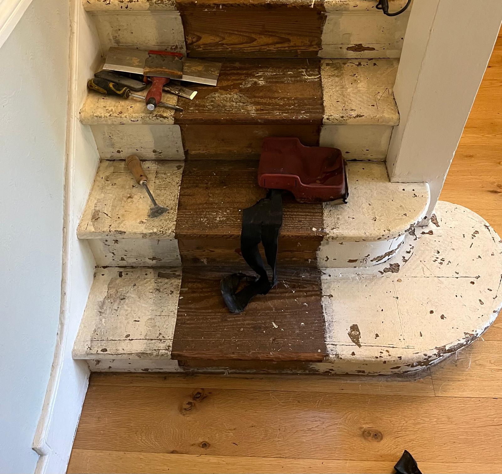 Partially stripped timber staircase during Staircase Sanding in London, showing worn painted pine wood treads, dark stained centre steps and sanding tools on the stair floor.