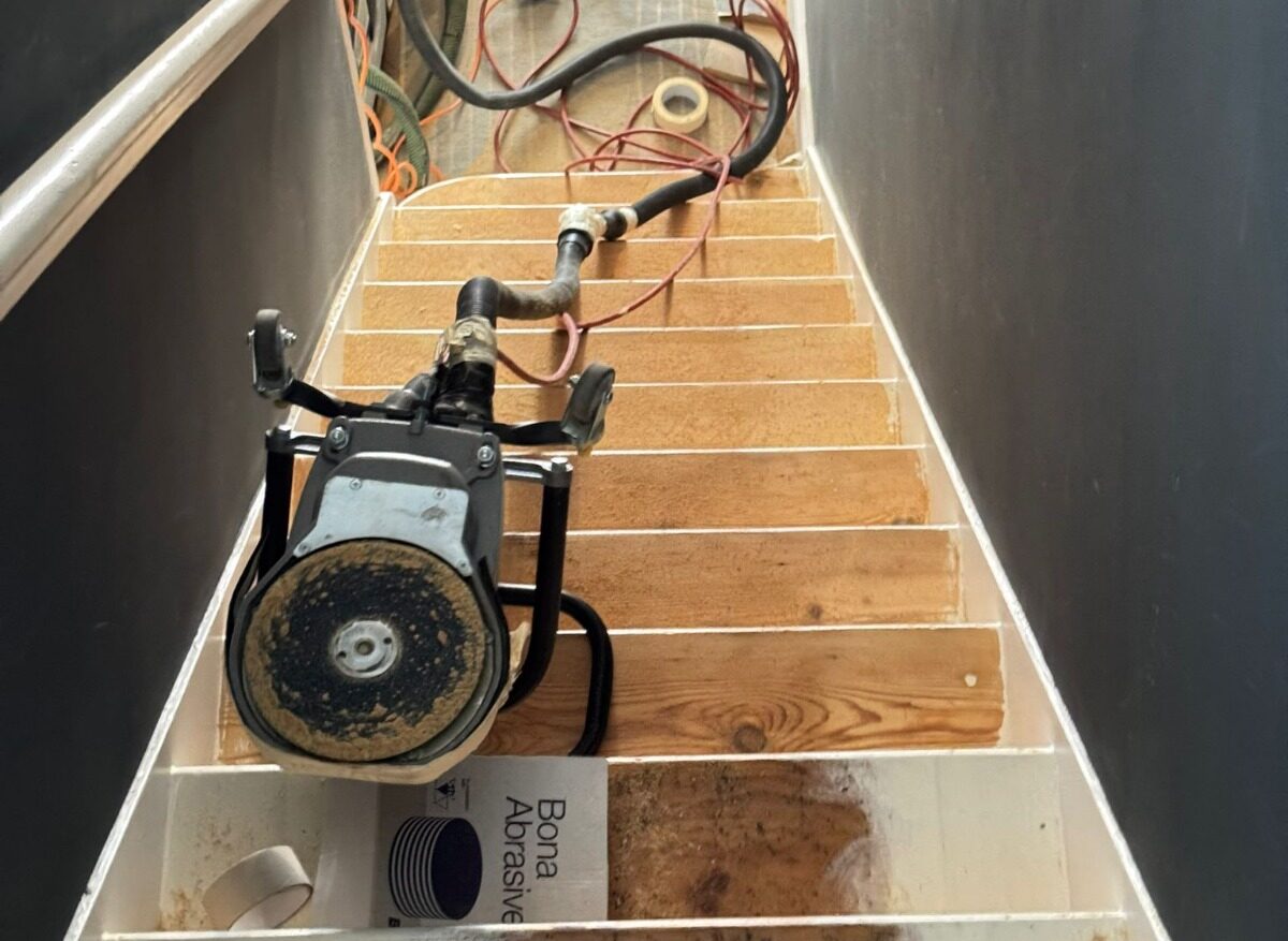 Professional Staircase Sanding in London in progress on pine wood staircase treads, showing sanding machine, dust extraction and partially stripped softwood steps.