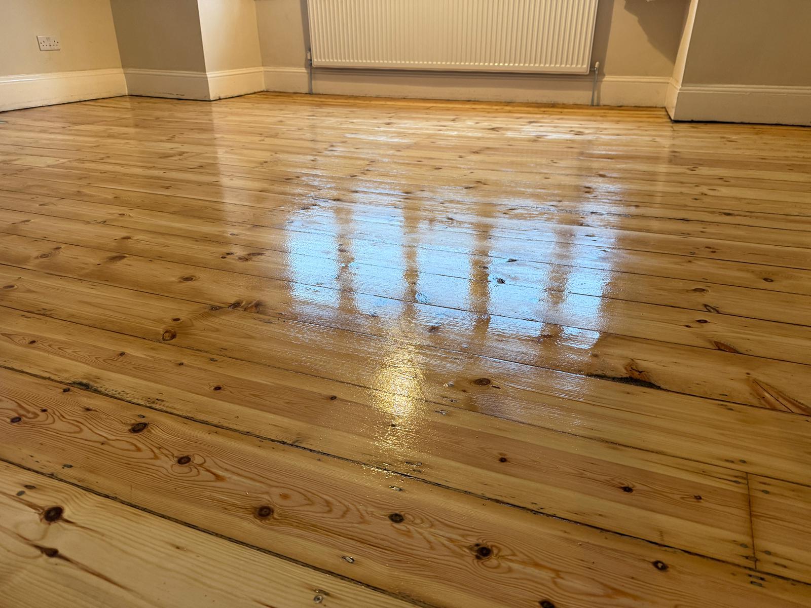 Timber Floor Restoration on solid pine softwood floorboards, freshly sanded and lacquered to a smooth, glossy finish in a bright empty room.