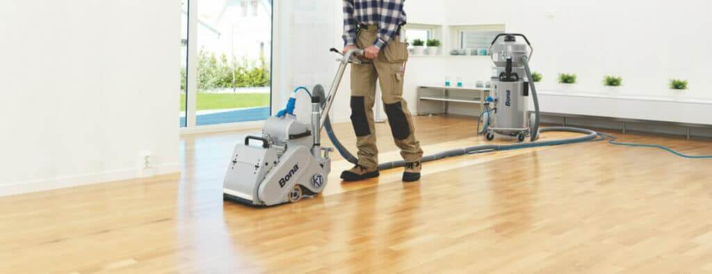 A technician from Mr. Sander® is sanding an oak wood floor in a living room in A technician from Mr. Sander® is sanding an oak wood floor in a living room using a Bona Belt (AMO110000.3) machine. The professional belt sander features a motor power of 2.2 kW, operates at 230 V and 50 Hz, with a sanding belt size of 200 x 750 mm or 250 x 750 mm. The machine has a drum width of 200 & 250 mm and a total weight of 74 kg. Additionally, the Bona DCS 70 dust containment system is used, featuring a 70 L dust holding capacity, HEPA filter, and 7.5 m hose, ensuring a clean and efficient sanding process. using a Bona Belt (AMO110000.3) machine. The professional belt sander features a motor power of 2.2 kW, operates at 230 V and 50 Hz, with a sanding belt size of 200 x 750 mm or 250 x 750 mm. The machine has a drum width of 200 & 250 mm and a total weight of 74 kg. Additionally, the Bona DCS 70 dust containment system is used, featuring a 70 L dust holding capacity, HEPA filter, and 7.5 m hose, ensuring a clean and efficient sanding process.