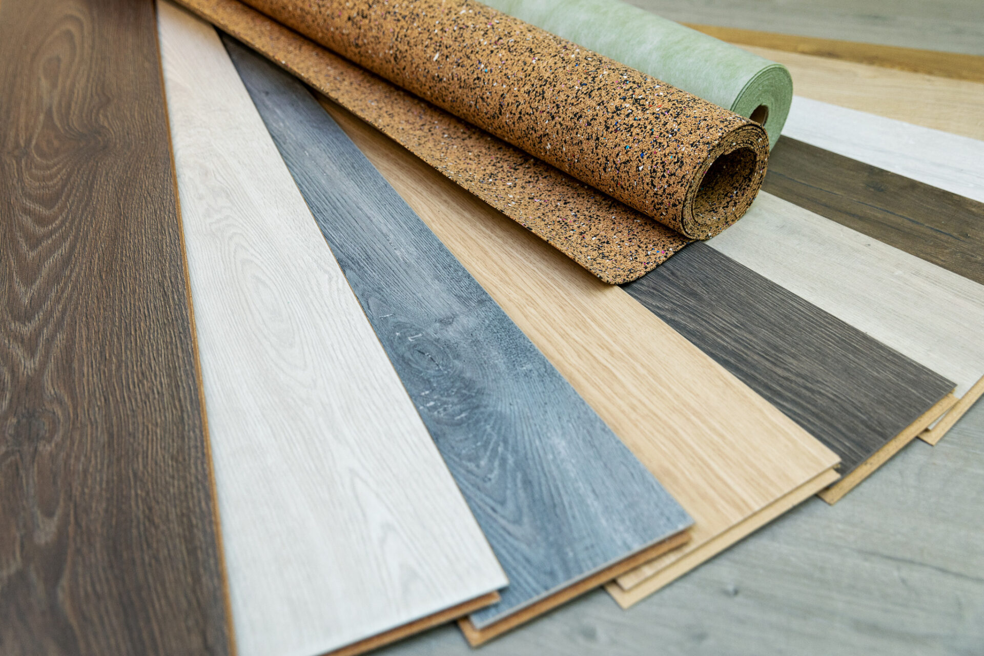 Underlay 101 showing cork and green foam rolls laid across samples of oak and grey engineered wood floors, demonstrating different underlay options for timber flooring.