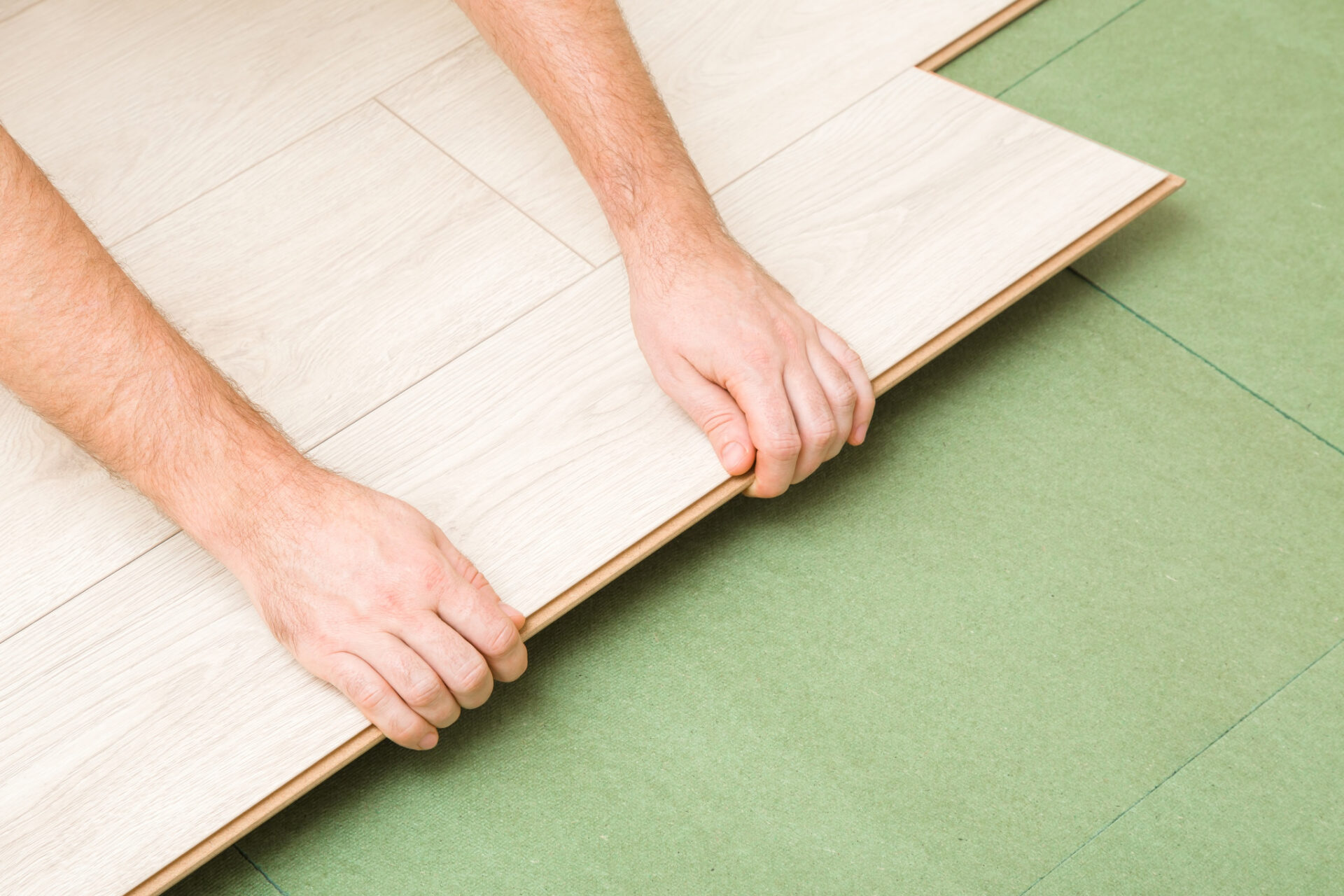 Underlay 101 showing a fitter locking light oak engineered wood floor planks into place over green fibreboard underlay.