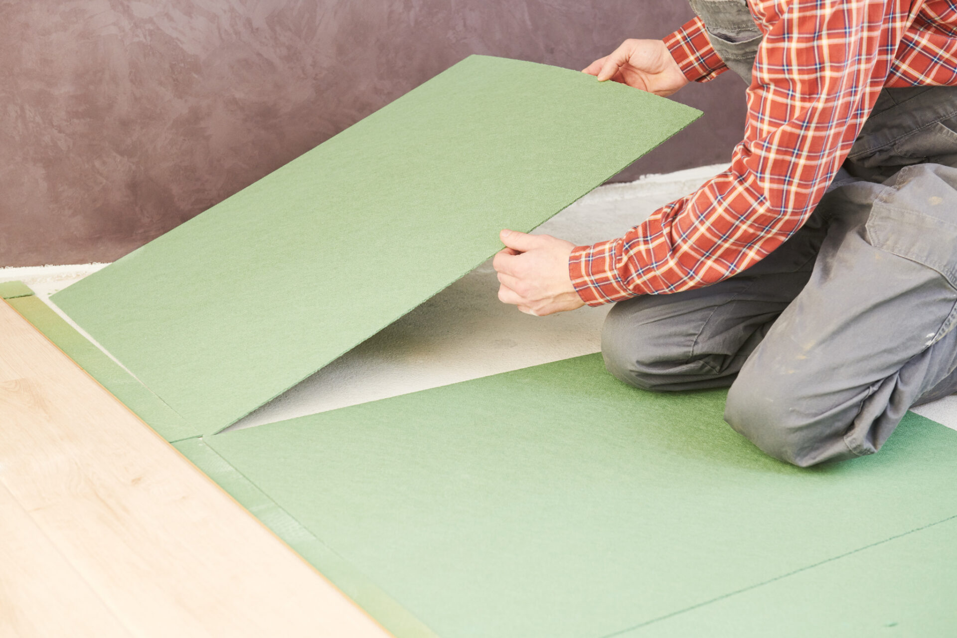Underlay 101 showing a fitter laying green fibreboard underlay panels beside a newly installed light oak engineered wood floor.