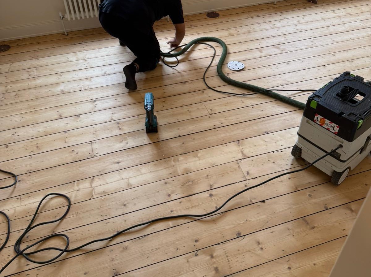 A professional worker sanding and restoring original Victorian floorboards London made of natural pine softwood.