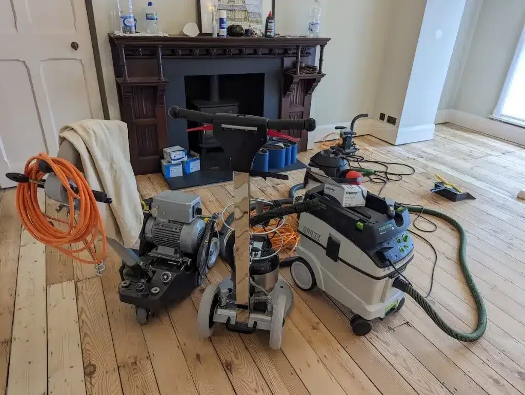 Dustless sanding setup on a Victorian Pine Floor—professional belt sander, edge sander and extractor placed on softwood pine floorboards during restoration.
