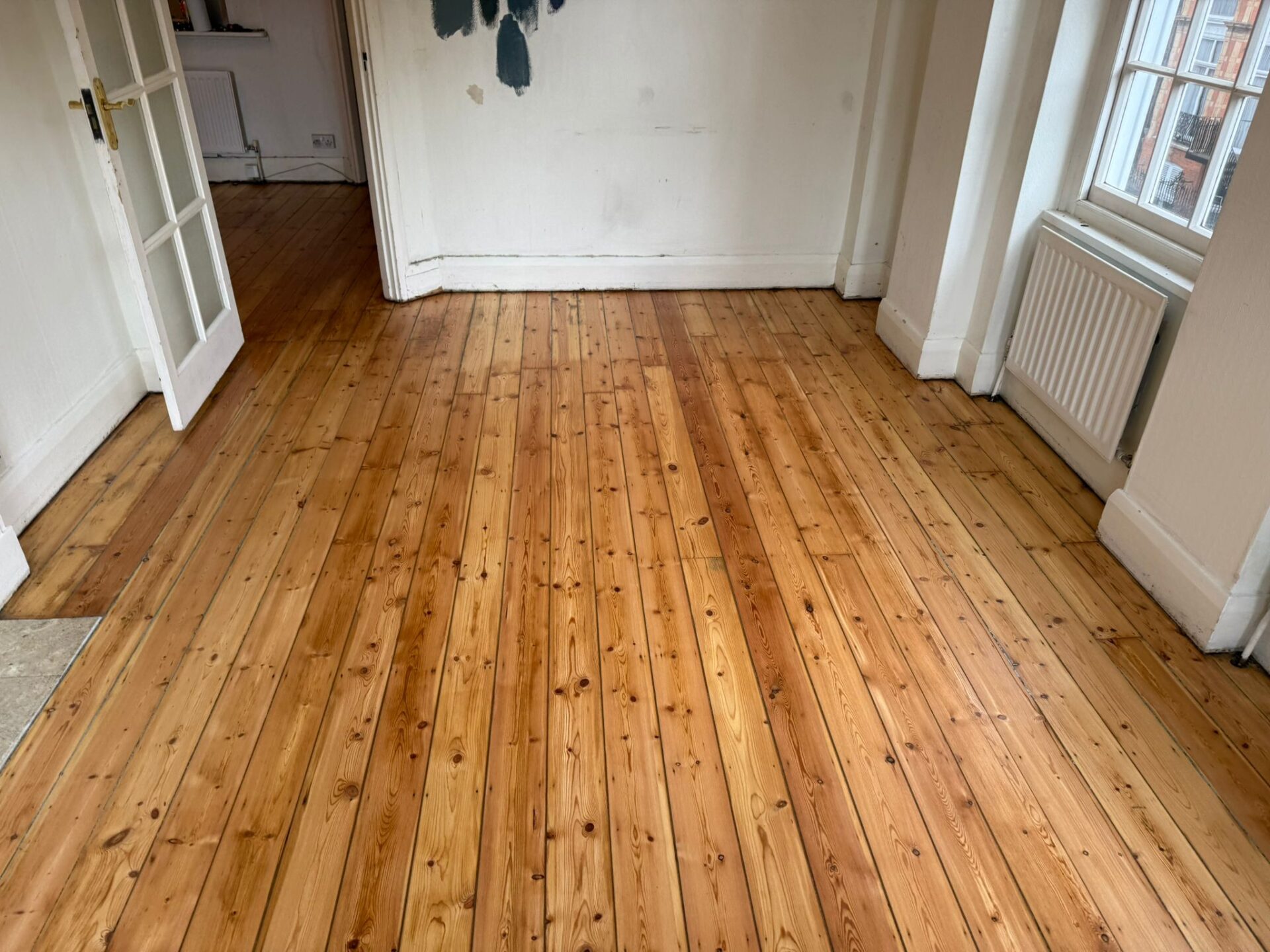 Victorian Pine Floor restored—sanded and sealed softwood pine floorboards with filled nail holes and a calm, matt-looking finish in a bright room.