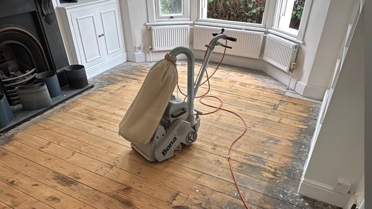 Victorian Pine Floor sanding in progress—professional belt sander with dust bag on original softwood pine boards, edges still showing old finish.