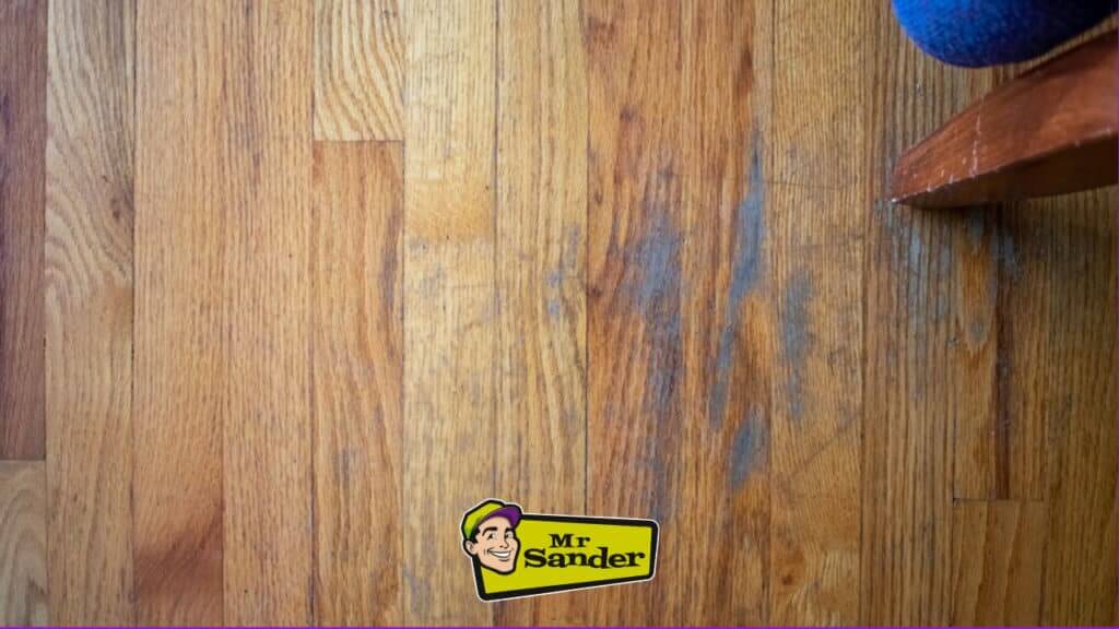 A close-up of a damaged hardwood floor with a watermark of Mr. Sander's logo.