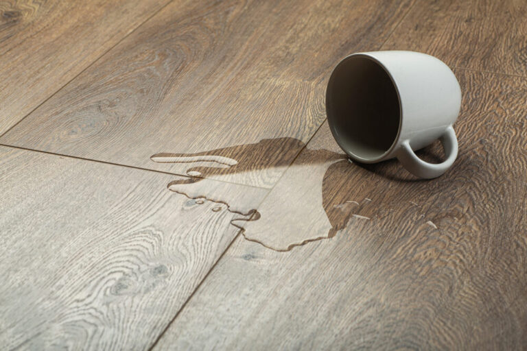 Overturned white mug with water puddling on a waterproofed oak floor, illustrating spill resistance after floor installation for waterproofing.