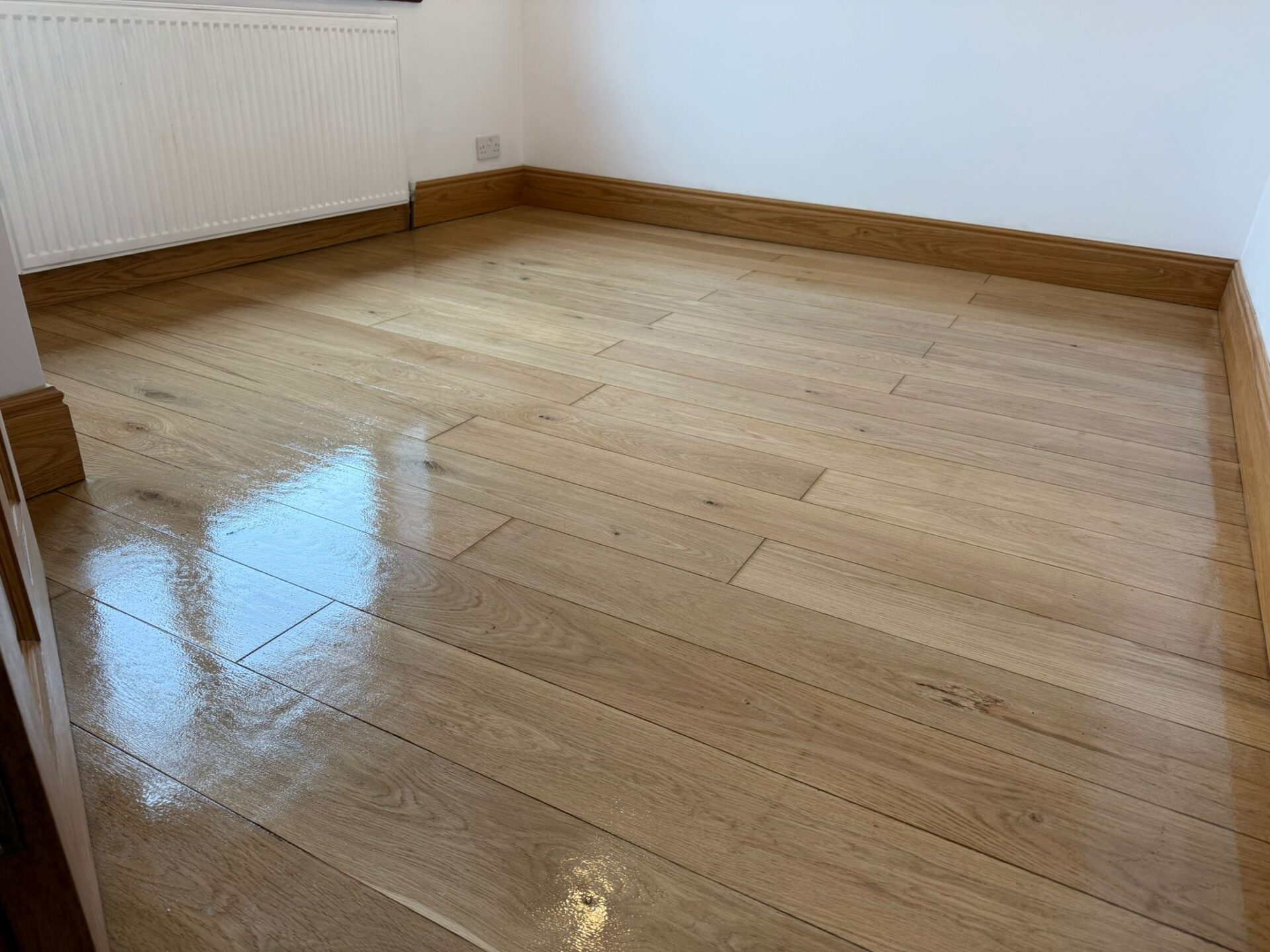 A room featuring wide-plank white oak engineered wood flooring that has just undergone buffing and polishing, showing a high-gloss reflective shine and natural wood grain.
