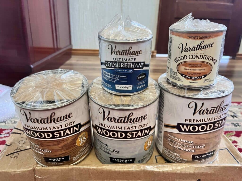 Cans of Varathane wood stain and conditioner on a cardboard box.