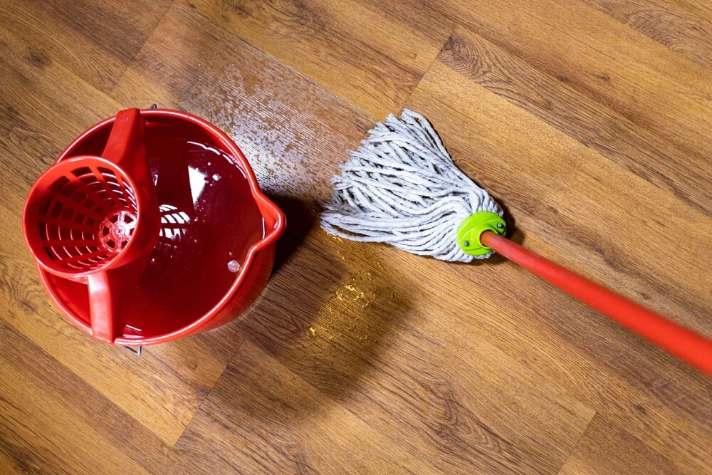 A red mop bucket and a mop on a freshly cleaned wooden floor with a polished finish.