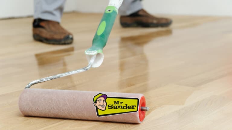 A close-up of a refinishing roller applying a glossy finish to a wooden floor by Mr. Sander®.