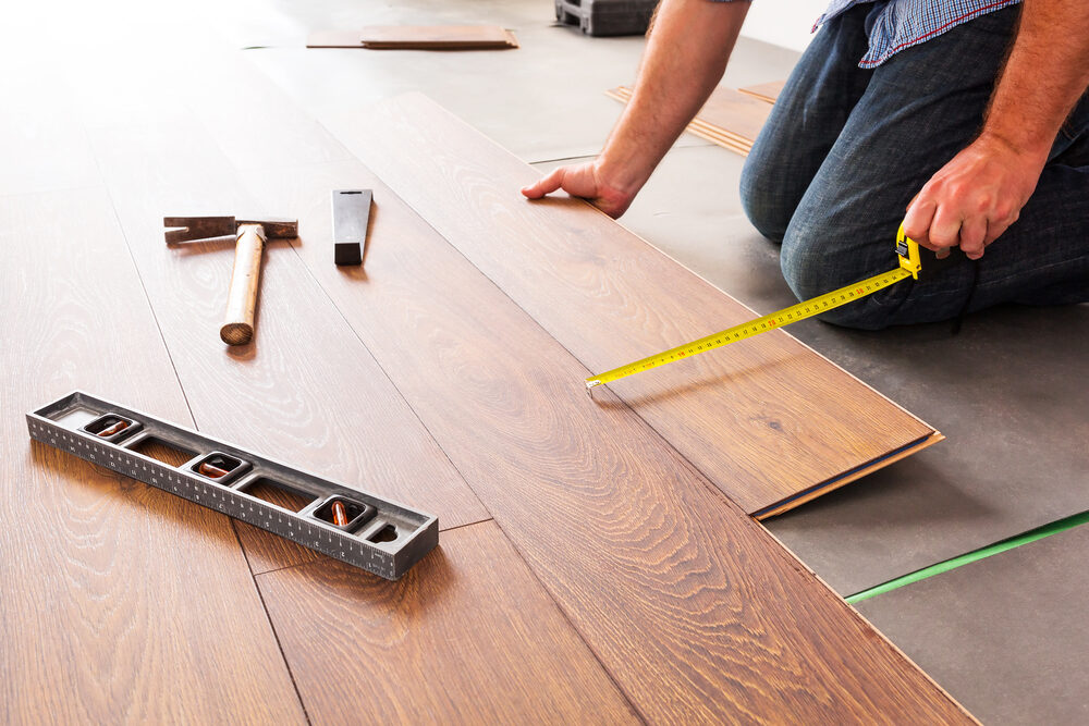 Close-up of a craftsman measuring and aligning engineered oak planks during a precise Wood Floor Fitting process.