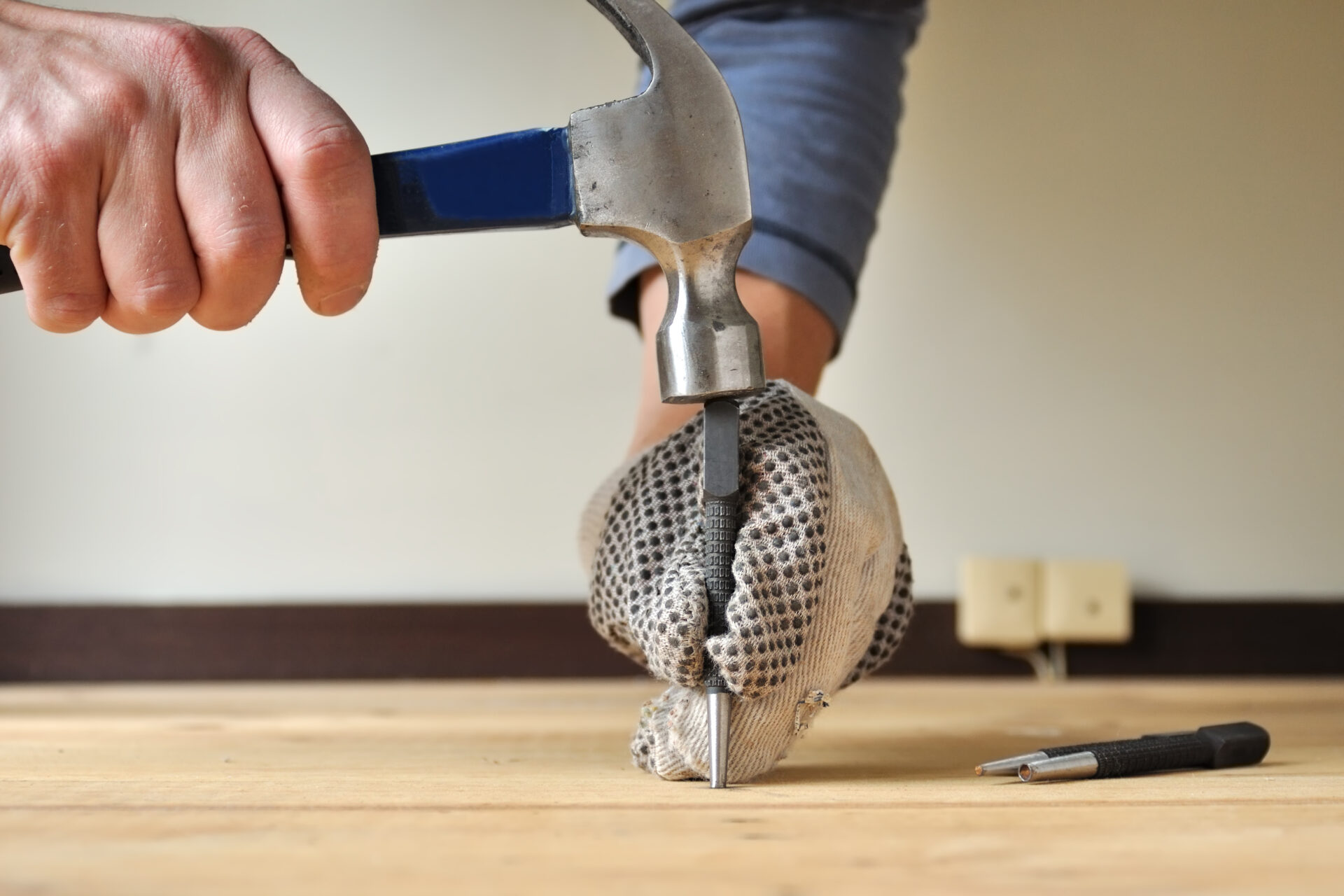 Wood Floor Repair on solid oak floorboards—technician countersinks a raised nail with a nail set and hammer to secure squeaky hardwood planks before sanding.