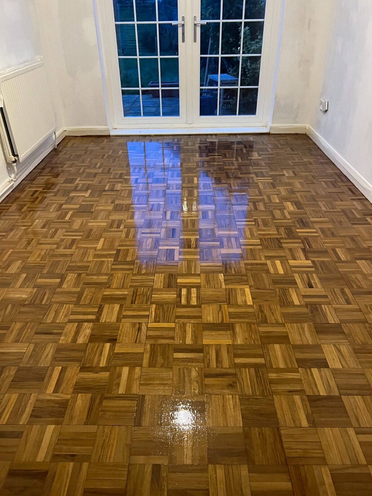 Wood Floor Restoration on oak finger-block parquet (hardwood), freshly lacquered to a high-gloss finish with clear grain and even sheen.