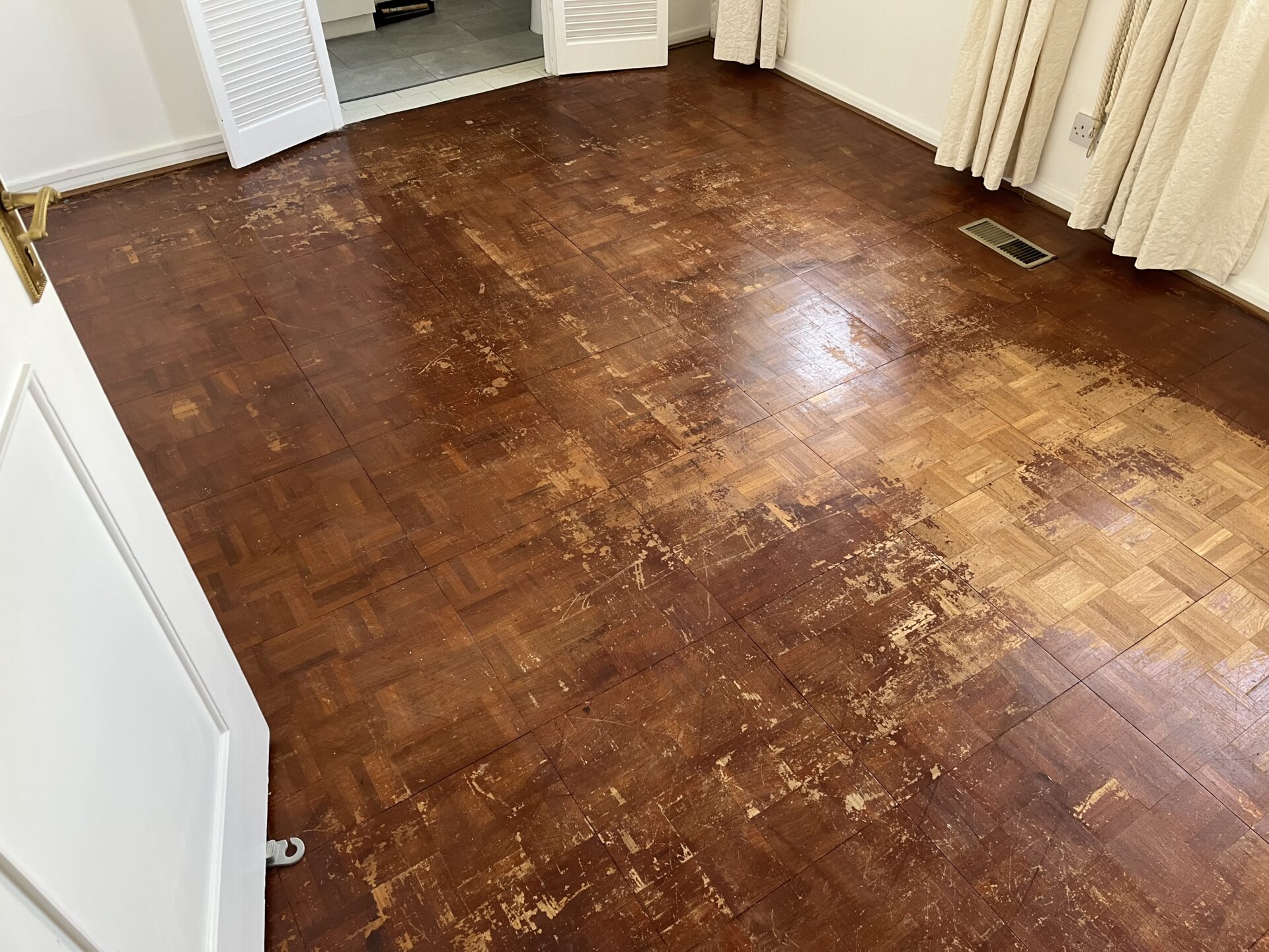 A heavily scratched and worn oak finger block parquet floor in a bedroom before undergoing professional wood floor sanding.