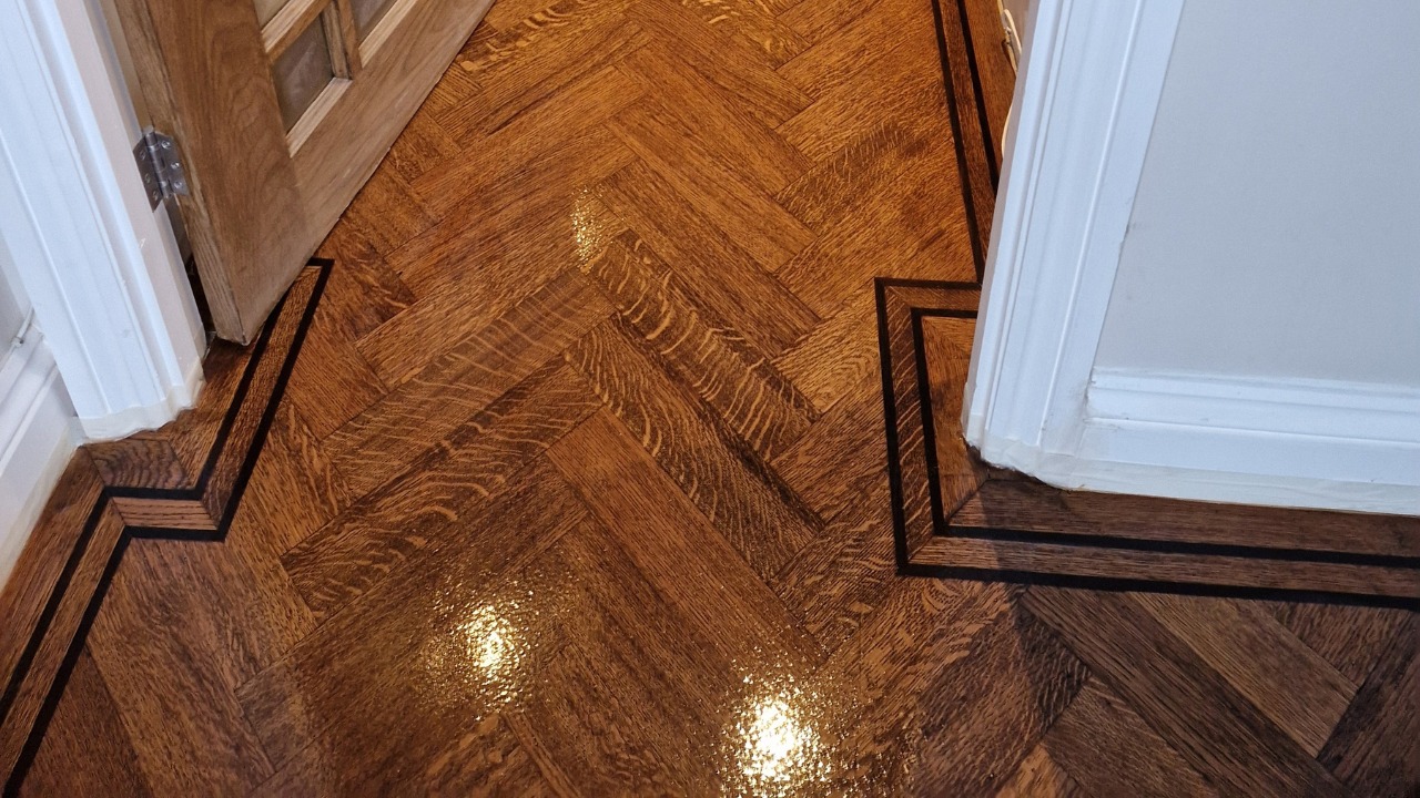Freshly refinished dark oak herringbone parquet wood floor with double border strips in a hallway after professional Wood Floor Sanding