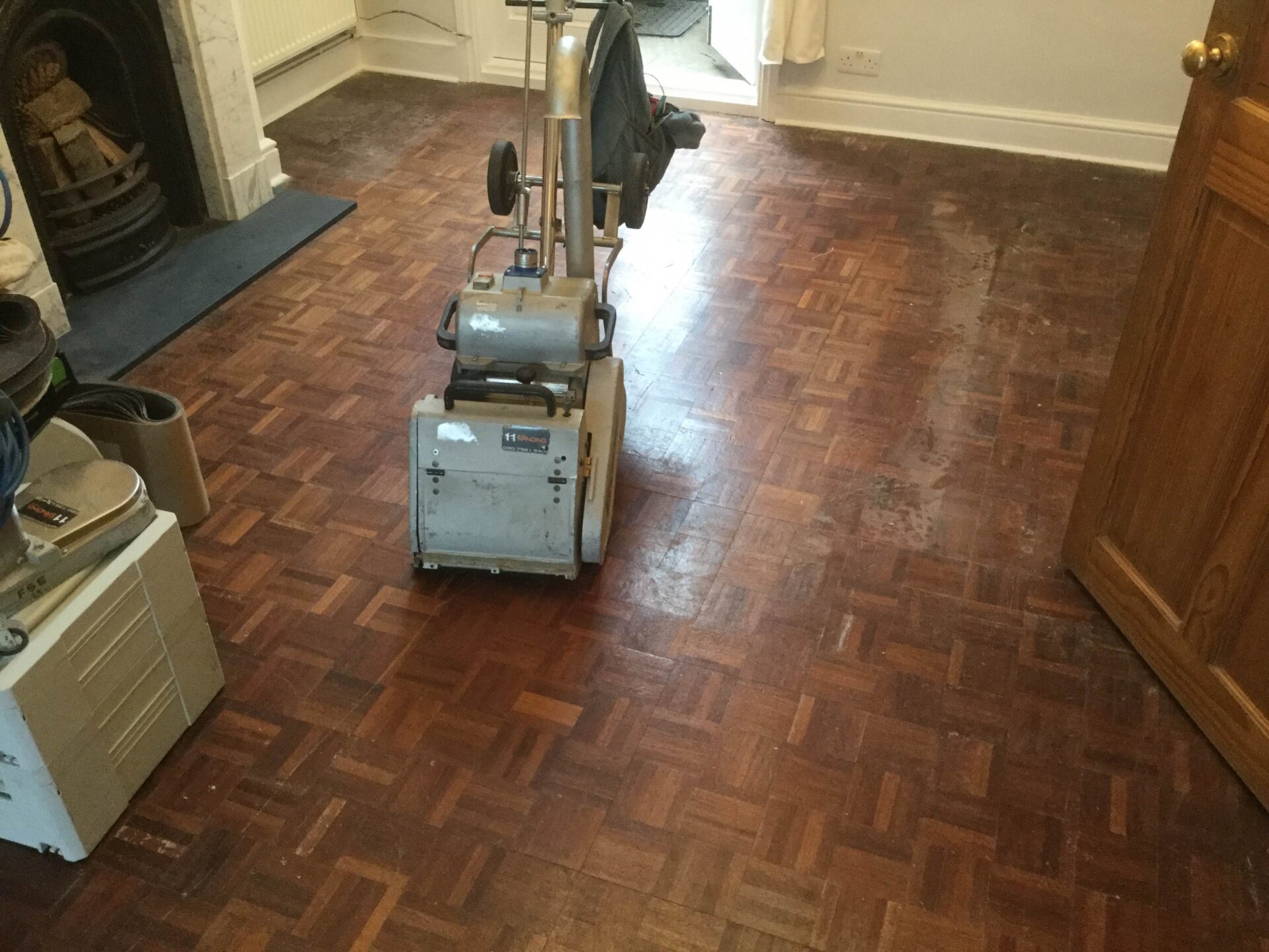 Londra'da, geleneksel bir oturma odasındaki meşe parke zemin üzerinde Ahşap Zemin Zımparalama işlemi yapılıyor ve tamburlu zımpara makinesi, yıpranmış parke bloklarını tamir için hazırlıyor.