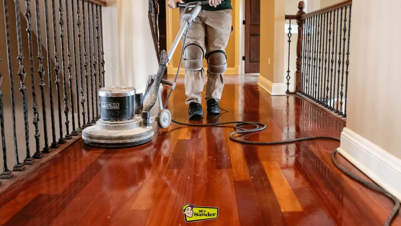 A professional sanding and polishing a deep red-toned hardwood floor in a hallway, showcasing floor restoration by Mr. Sander in Northwick Park.