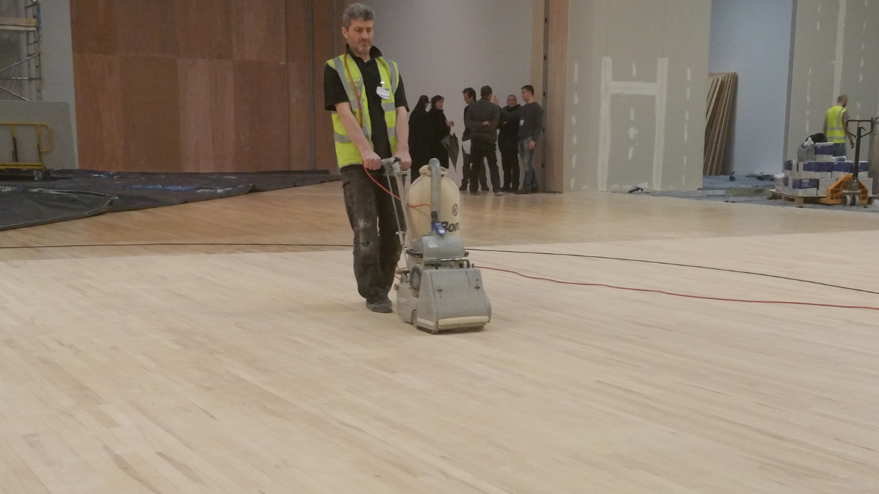 Professional Wood Floor Sanding on a large maple hardwood sports floor in a commercial hall using an industrial belt sander