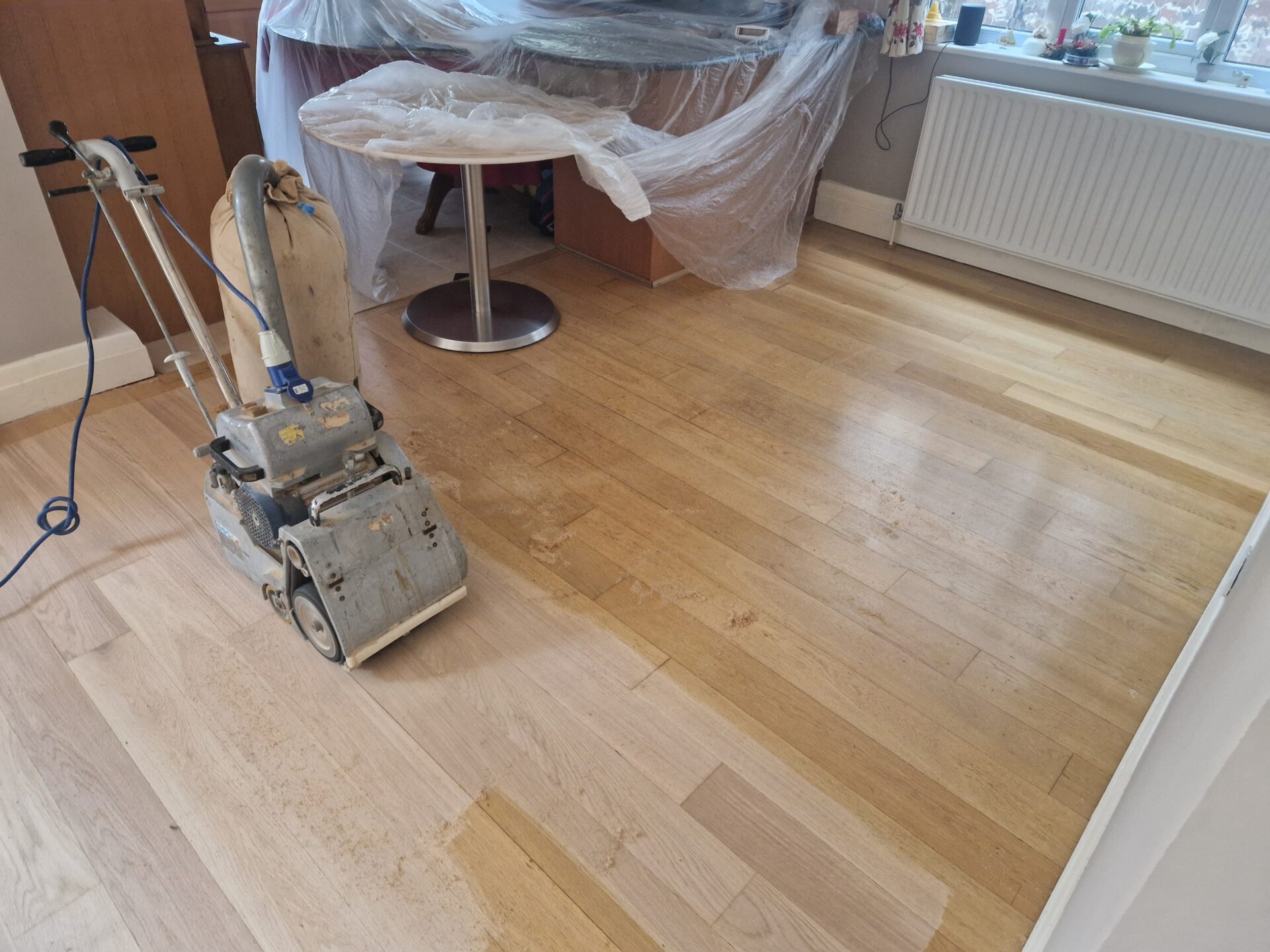 Wood Floor Sanding in progress on an oak hardwood plank floor, showing the contrast between the freshly sanded pale boards and the older, worn finish in a kitchen-diner.