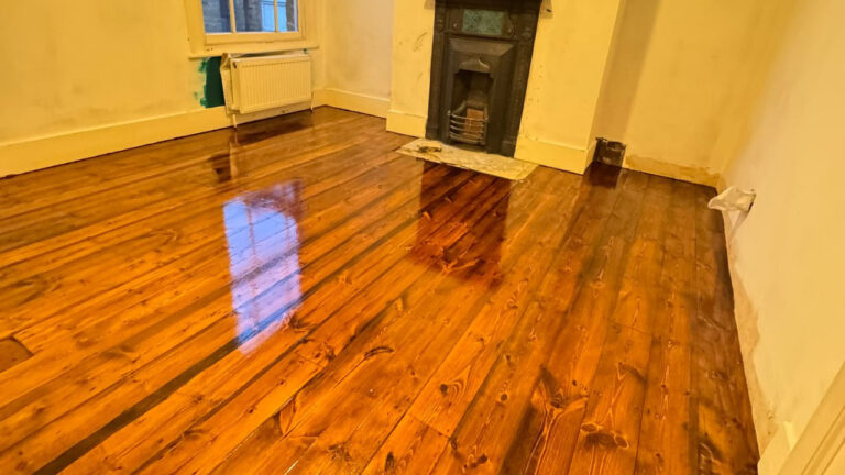 Wood Floor Sanding results on original pine floorboards, showing a rich, dark-stained softwood plank floor with a high-gloss finish in a period room with fireplace.