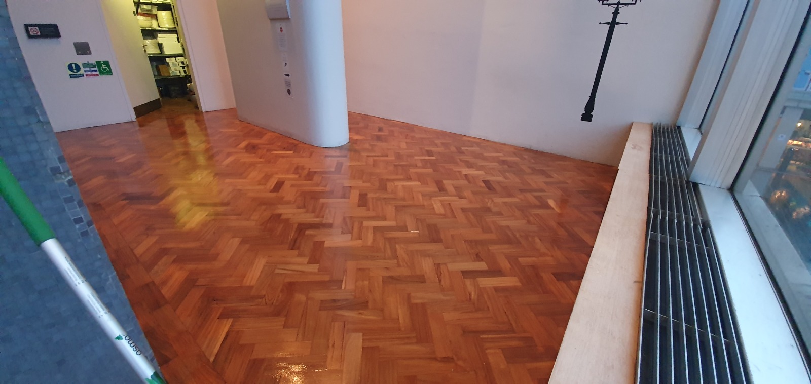 Wood Floor Staining on an oak herringbone parquet hardwood floor, creating a rich, glossy finish along a modern corridor.
