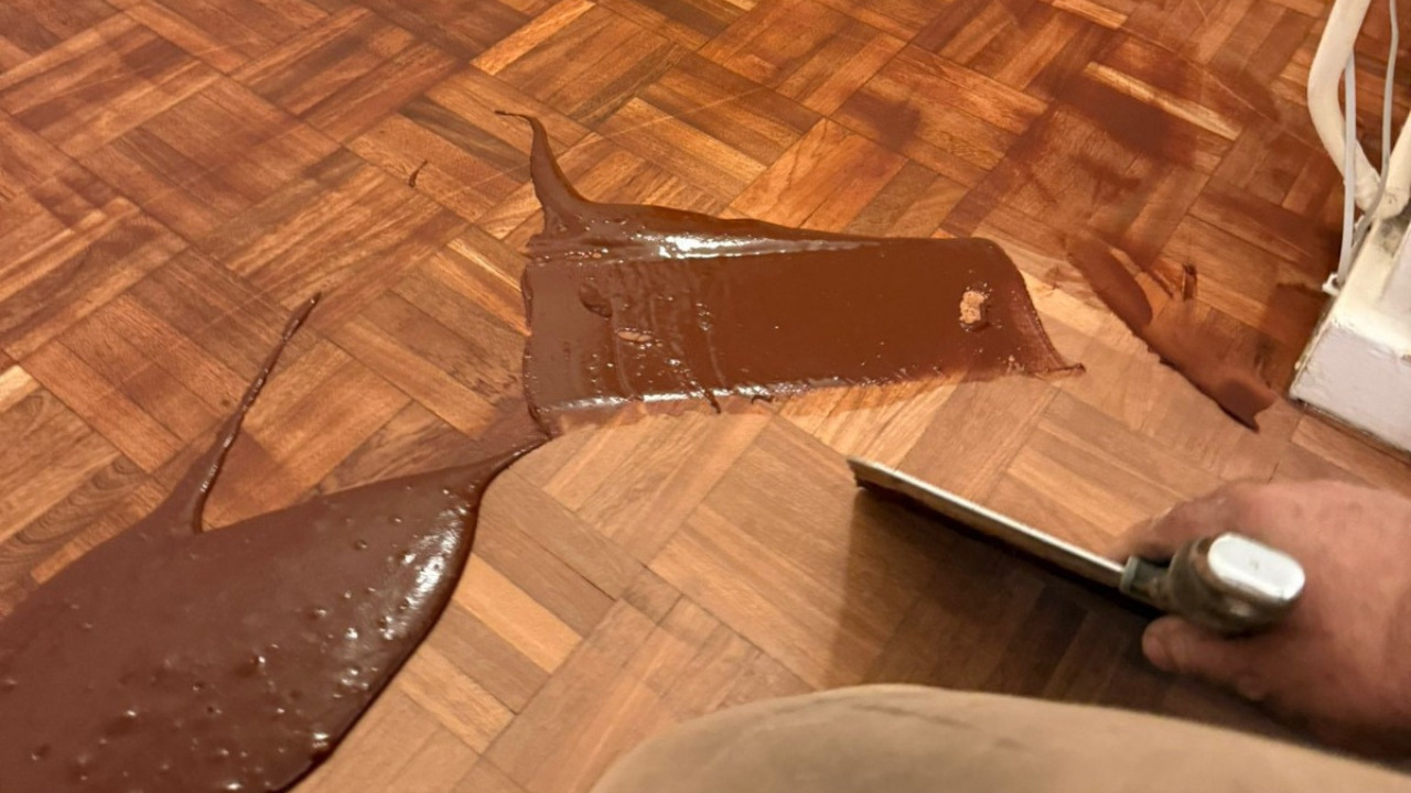 Pürüzsüz, eşit bir yüzey elde etmek için blokların arasına el kazıyıcı kullanılarak renkli dolgunun uygulandığı meşe parke ahşap zemin üzerinde Profesyonel Ahşap Zemin Boyama çalışması.