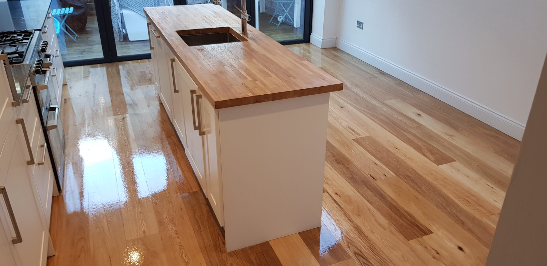 Worktop Sanding in London showing a freshly refinished solid oak island worktop and matching engineered oak plank floor with a smooth, glossy finish in a bright kitchen.