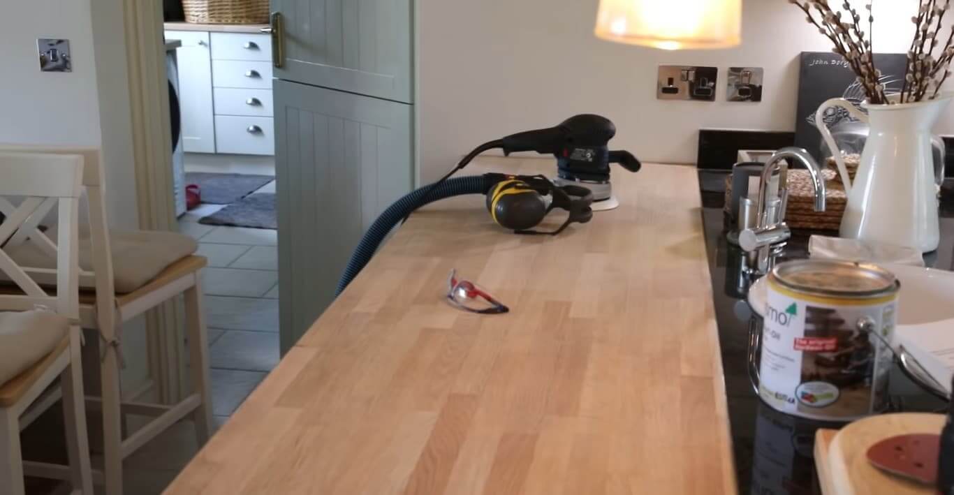 Worktop Sanding in London in progress on a solid oak block kitchen worktop, with tools, safety goggles and finishing oil on display beside an oak parquet wood floor.