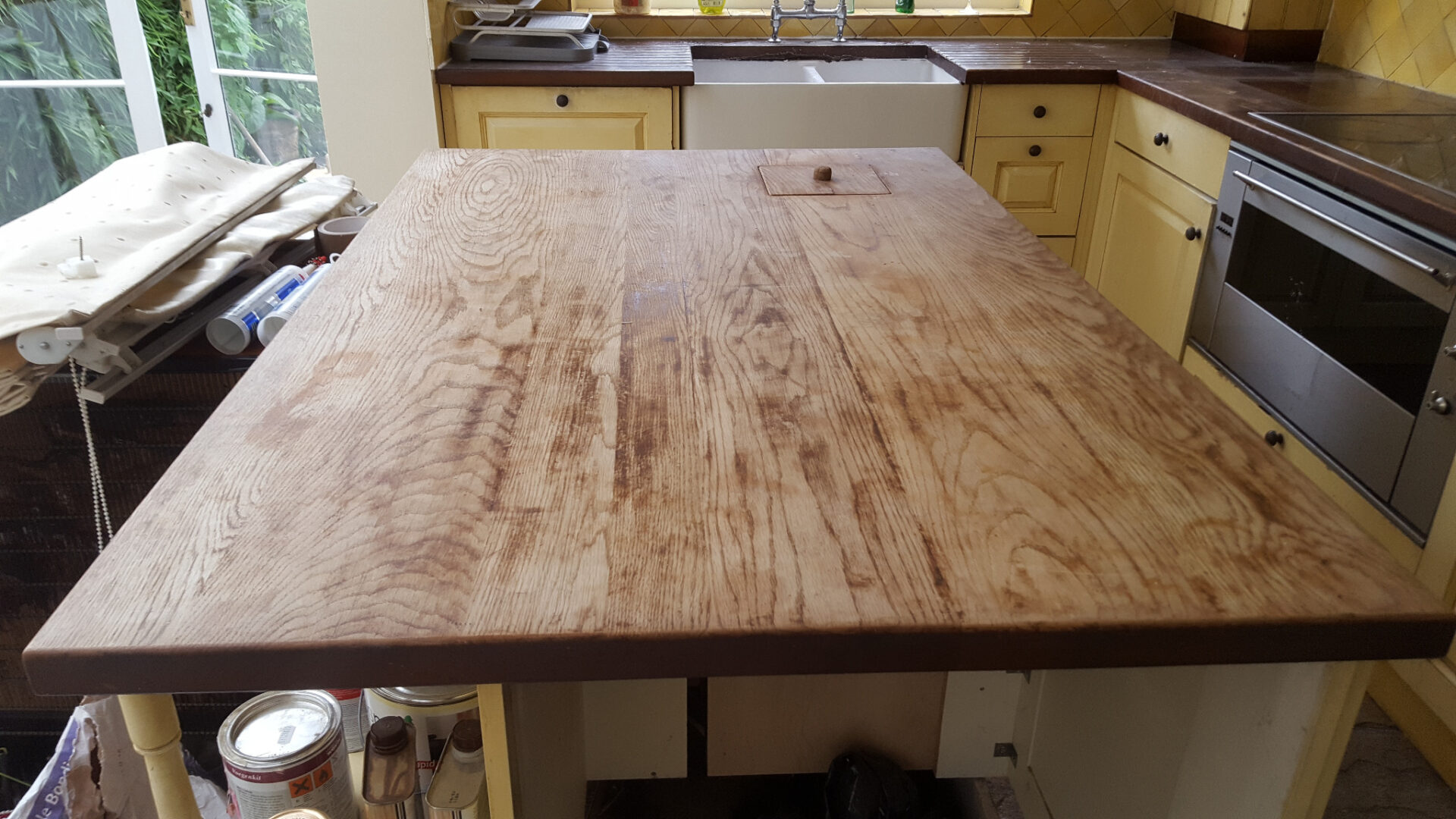 Worktop Sanding in London shown on a worn solid oak island worktop before restoration, with an oak plank wood floor beneath ready to be refreshed.